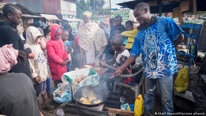 A man cooks while others watch in Mandazi, Kenya