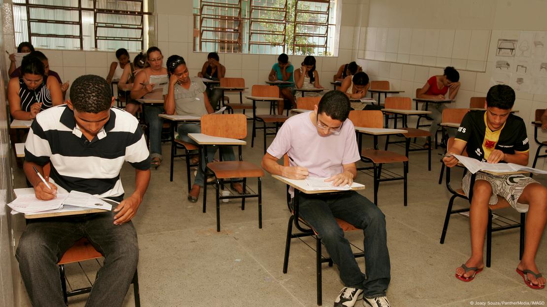 Alunos sentados separados em sala de aula escrevendo prova