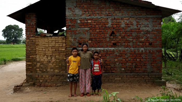 Parwati Sunar stands in front of her brick house with her sons Resham and Arjun.