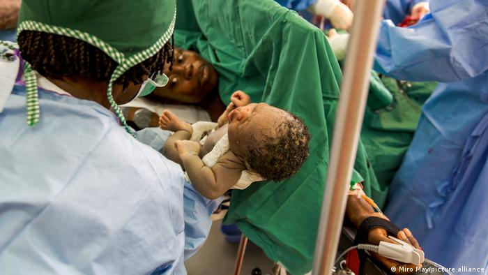 A newborn baby in the arms of a medic while the mother looks on