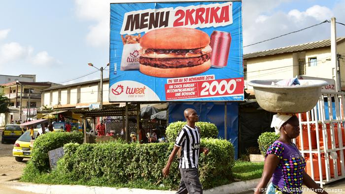 People walk past a restaurant board advertising for a two krika menu (two krika is equivalent to 2000 CFA francs) in Nouchi language, a slang used by many Ivorians