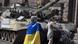 Женщина в украинском флаге на фоне подбитого танка Женщина в украинском флаге на фоне подбитого танка