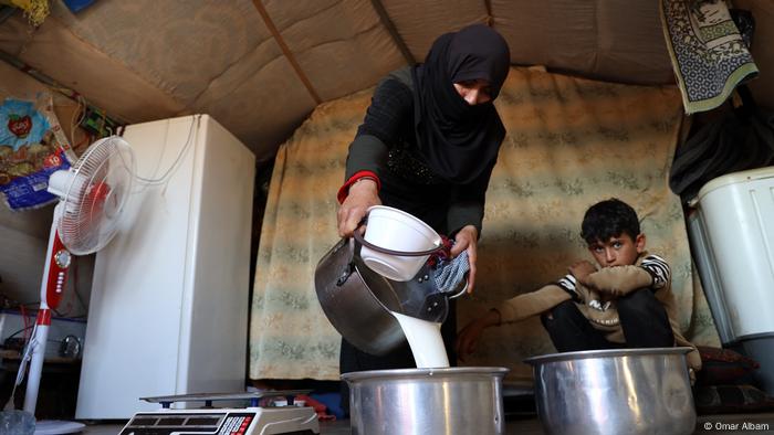 Syrian woman Moufida Rahmoun is preparing milk for sale while a boy looks on