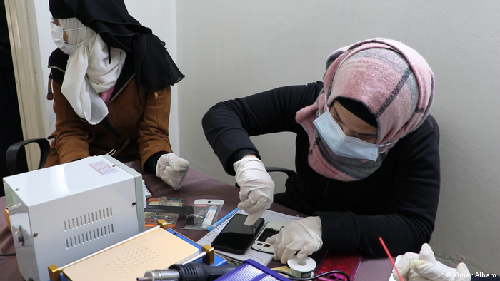 Syrian women are repairing phones with tools, wearing masks and gloves