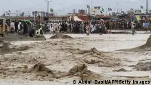 TOPSHOT - People wade through flooded mud water after heavy monsoon rainfall in the border town of Chaman in Balochistan province on August 25, 2022. - Figures from the national disaster agency showed on August 25 that 903 people had died in the floods since June, and over 180,000 were forced to flee their rural homes. (Photo by Abdul BASIT / AFP) (Photo by ABDUL BASIT/AFP via Getty Images)