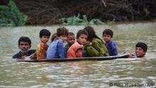 TOPSHOT - A man (L) along with a youth use a satellite dish to move children across a flooded area after heavy monsoon rainfalls in Jaffarabad district, Balochistan province, on August 26, 2022. - Heavy rain continued to pound parts of Pakistan on August 26 after the government declared an emergency to deal with monsoon flooding it said had affected over four million people. (Photo by Fida HUSSAIN / AFP)