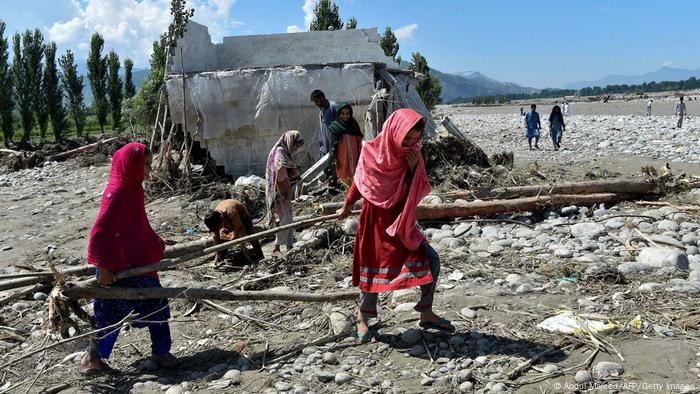 Two women in Mingora, Swat Valley, carry wood near a damaged house