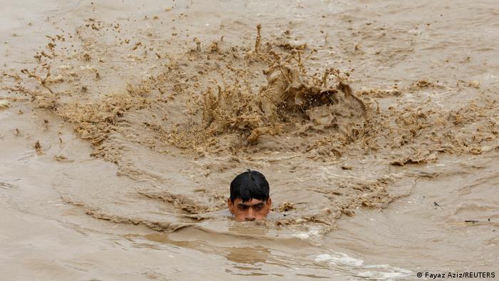 A man swims through brown floodwater, with only his head visible above the deluge