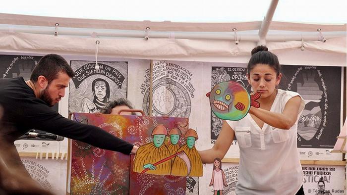 Two actors perform a play on forced disappearances while holding hand puppets and drawings.