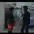 Filmstill aus 'Black Chariot': ein Mann und eine Frau stehen vor einer Hauswand mit Postern und unterhalten sich 