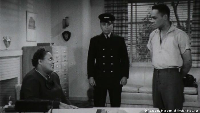 A film still from 'Reform School': A sitting woman looks up at two men, one of them wearing a uniform.