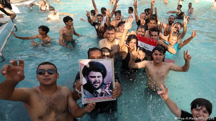 A young man jumps in the pool. They hold in their hands a picture of the Shiite leader Sadr.