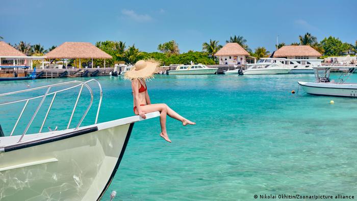 Frau in rotem Bikini sitzt auf einem Schiffsbug vor türkisblauem Meer auf den Malediven