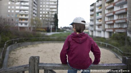 Un enfant seul au bord d'un parc pour enfant bordés d'immeubles