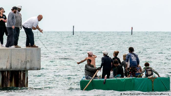 Personas en un muelle ayudan a llegar a una embarcación improvisada con migrantes dentro.