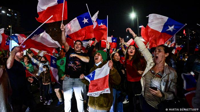 Personas con banderas de Chile celebran en una plaza.