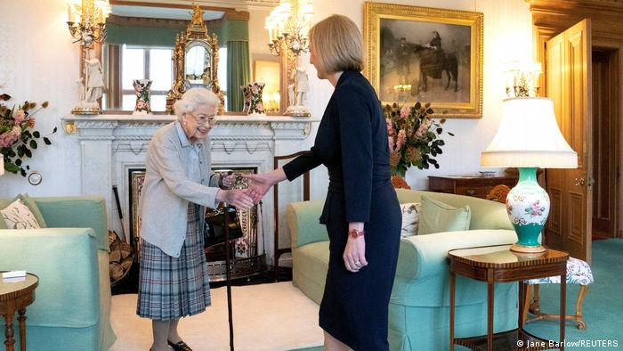 Die Queen reicht Liz Truss in einem altmodisch eingerichteten Zimmer mit Kamin die Hand.