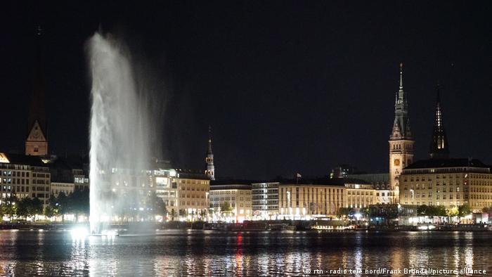 Der große Springbrunnen fließt über, während Hamburg nachts im Hintergrund leuchtet.