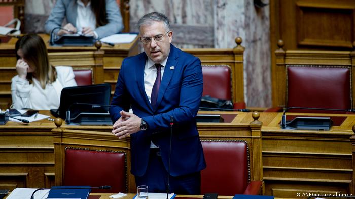 Zdjęcie przedstawia Takisa Theodorikakosa stojącego przed mikrofonem i przemawiającego w greckim parlamencie
