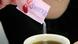 A person pours a pack of Sweet 'N Low, a sugar substitute, into a drink