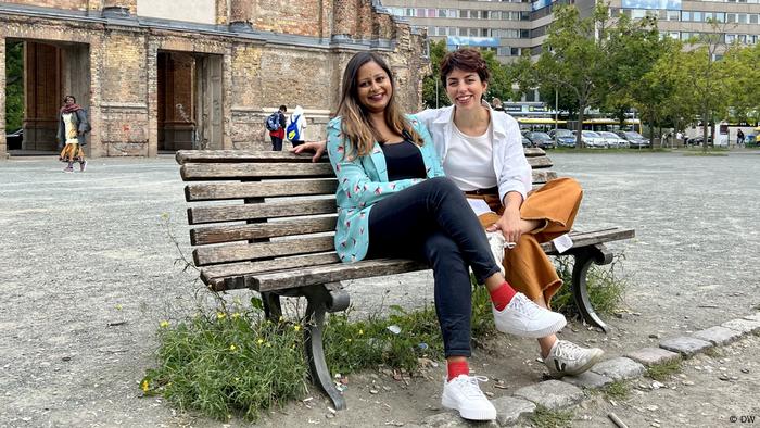 Laila Abdalla and Shabnam Surita sit on a bench in front of Anhalter Bahnhof in Berlin.