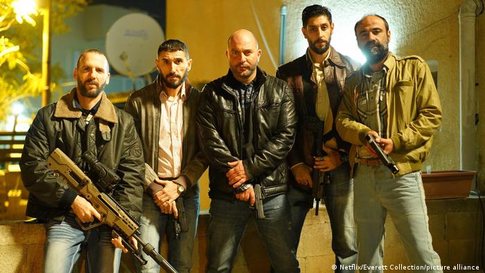 Five armed men stand in a row in front of the camera.  A scene from the Netflix series Fauda.