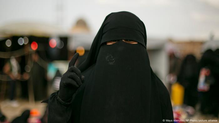 A woman poses for a portrait at Al-Hol camp, holding up one finger. 