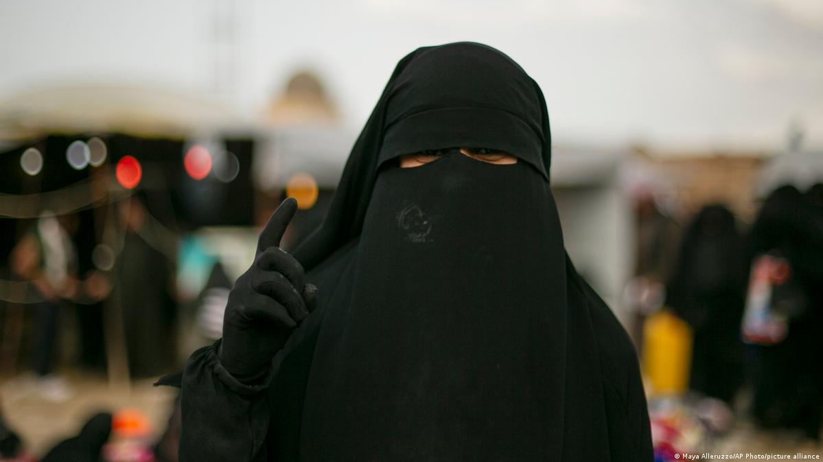 A woman poses for a portrait at Al-Hol camp, holding up one finger. 