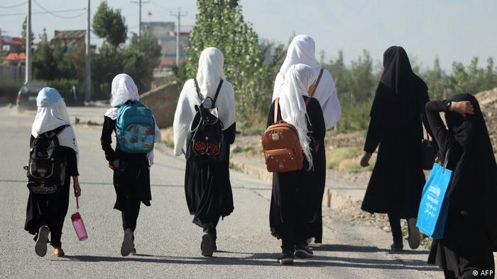 Eine Gruppe Mädchen von hinten fotografiert geht eine Straße entlang. Alle tragen dunkle Kleidung und entweder schwarze oder weiße Kopftücher.