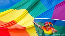 A participant at the Malta Pride Parade surrounded by a giant rainbow flag