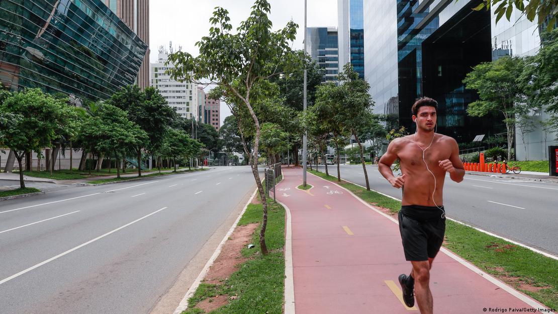 Homem sem camisa corre em ciclovia em avenida com predios comerciais.