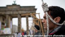 Exil-Iraner demonstrieren am 10.12.2013 vor dem Brandenburger Tor in Berlin mit symbolischen Galgen gegen Hinrichtungen und Steinigungen im Iran. Die Anhänger des Nationalen Widerstandsrats Iran (NWRI) setzen sich mit einem Hungerstreik für die Freilassung von sieben iranischen Oppositionellen im Irak ein. Foto: Bernd von Jutrczenka/dpa ++ +++ dpa-Bildfunk +++
