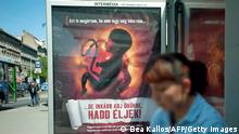 TO GO WITH AFP STORY BY ESZTER BALAZS- A woman waits in front of an anti-abortion poster bearing a picture of a foetus and slogan reading ''I can also understand if you are not yet prepared to receive me, but have me rather adopted and let me live! (down), on May 17, 2011 at a bus-stop in downtown Budapest. Hungary, the current EU president, came under fire from Brussels this week for using European money to fund an anti-abortion campaign. AFP PHOTO / BEA KALLOS / MTI (Photo credit should read BEA KALLOS/AFP via Getty Images)