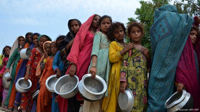 Displaced flood-affected people, holding pans, stand in a queue to receive food 