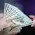 Foto simbólica de una persona que sostiene billetes de dólares en su mano.