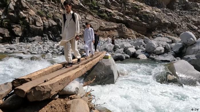 Dos jóvenes pakistaníes caminan sobre un madero colocado como puente provisorio sobre una correntada.
