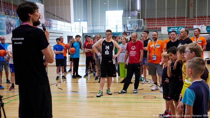 Basketball players listen to a man speaking into a microphone