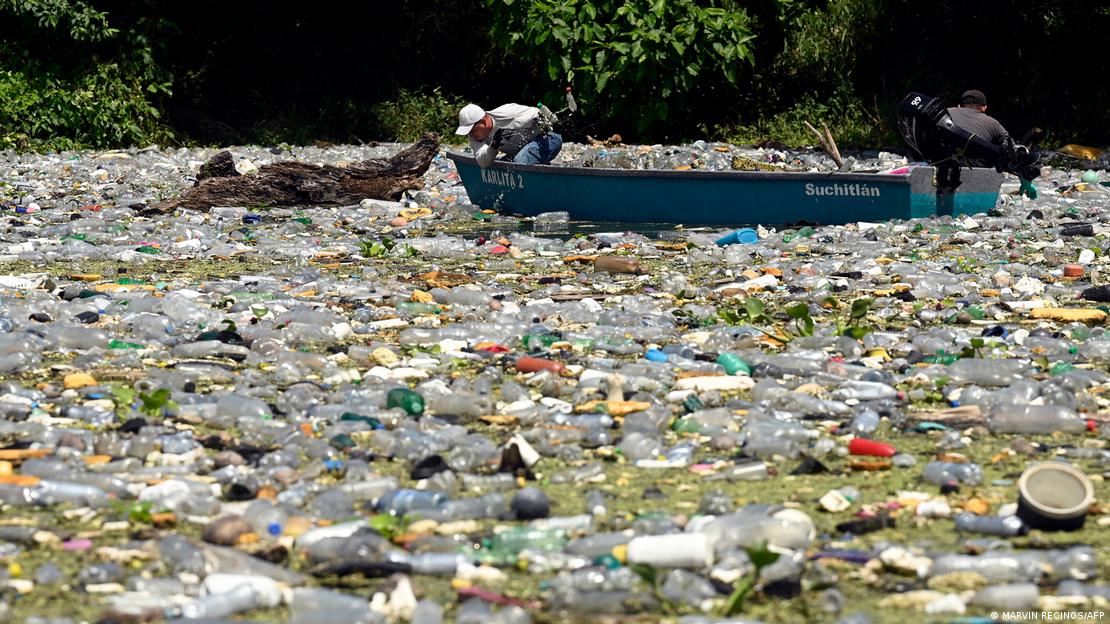Un hombre en medio del agua, completamente llena de residuos plásticos, en la represa de Cerrón Grande, El Salvador.