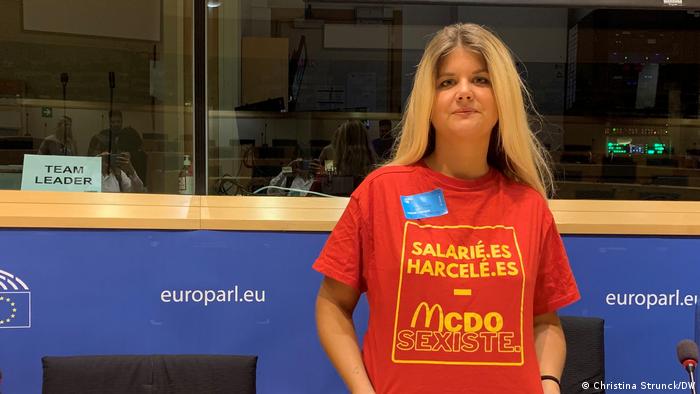 Young woman with blond hair presents her red T-shirt with the inscription McDo Sexiste