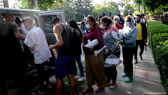 Migrantes se suben a minibuses tras ser llevados frente a la casa de Kamala Harris.