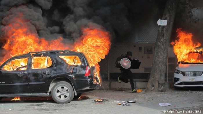 Foto de una persona que corre cerca de dos carros incendiados en Haití en una imagen de archivo.