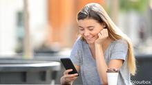 Happy teenage girl using a smart phone watching online content sitting in a park