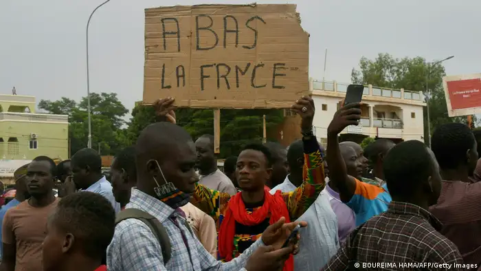 A man stands in a crowd holding a placard reading A Bas La France or Down with France