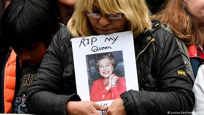 A woman holds a photo of Queen Elizabeth with the words: RIP my Queen