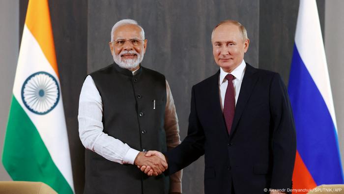 Wladimir Putin und Narendra Modi schütteln sich die Hand und lächeln in die Kamera, daneben die Flaggen ihrer Länder