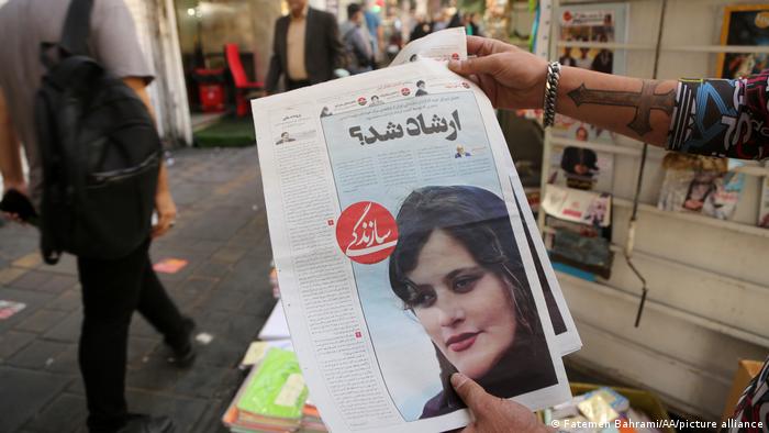 Hands holding up a newspaper bearing an image of Mahsa Amini.