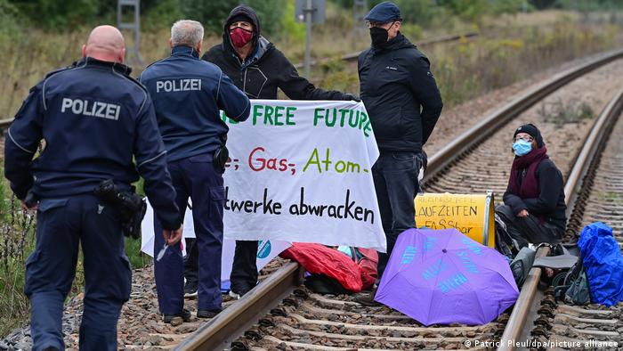 Two police officers approach three members of the public holding a large banner and obstructing a railway line near the Jänschwalde coal power plant in Brandenburg, eastern Germany. September 19, 2022.