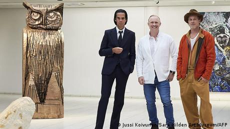 Nick Cave (let), Thomas Houseago (center) and Brad Pitt (right) stand together next to sculptures, one of which is a gian owl, in the Sara Hilden Art Museum.