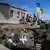 Soldaten mit ukrainischer Fahne fahren auf einem gepanzerten Fahrzeug über eine Dorfstraße