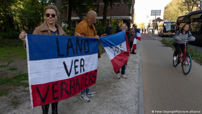 Des manifestants aux Pays-Bas tiennent des drapeaux nationaux griffonnés avec le mot «traître» à l'envers alors que des invités sont transportés en bus pour entendre le discours du roi